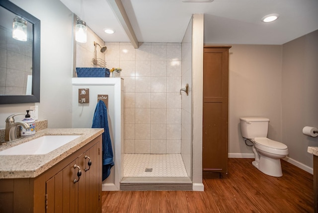 bathroom with hardwood / wood-style floors, a tile shower, vanity, toilet, and beamed ceiling