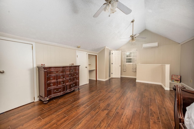 additional living space with dark wood-type flooring, vaulted ceiling, a textured ceiling, an AC wall unit, and ceiling fan