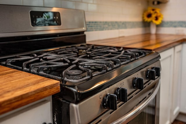 interior details with tasteful backsplash, gas range, butcher block counters, and white cabinets