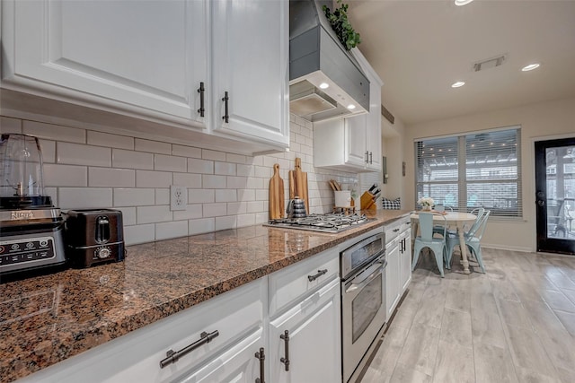 kitchen with white cabinetry, backsplash, stainless steel appliances, custom exhaust hood, and light wood-type flooring