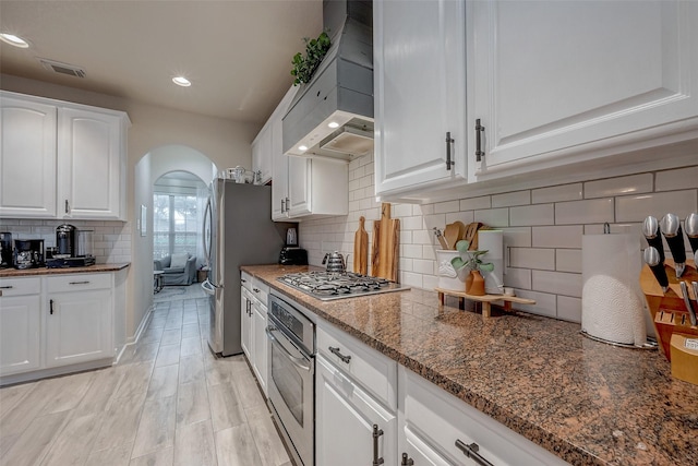 kitchen with decorative backsplash, appliances with stainless steel finishes, custom range hood, and white cabinets