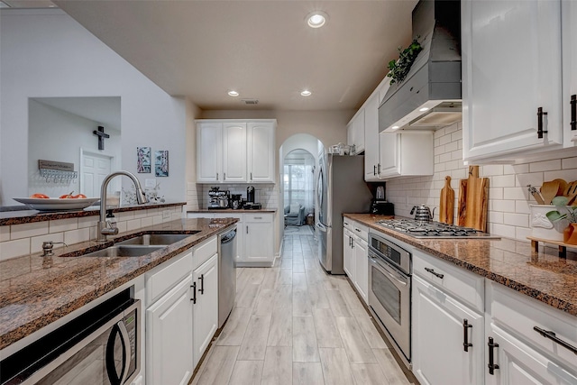 kitchen featuring premium range hood, sink, white cabinetry, dark stone countertops, and appliances with stainless steel finishes