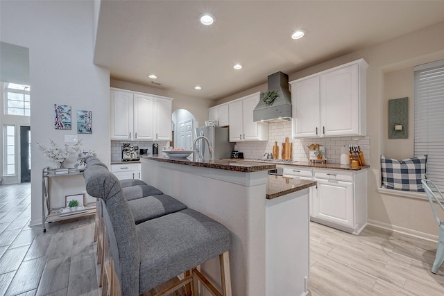 kitchen featuring custom exhaust hood, white cabinets, a breakfast bar area, and dark stone counters