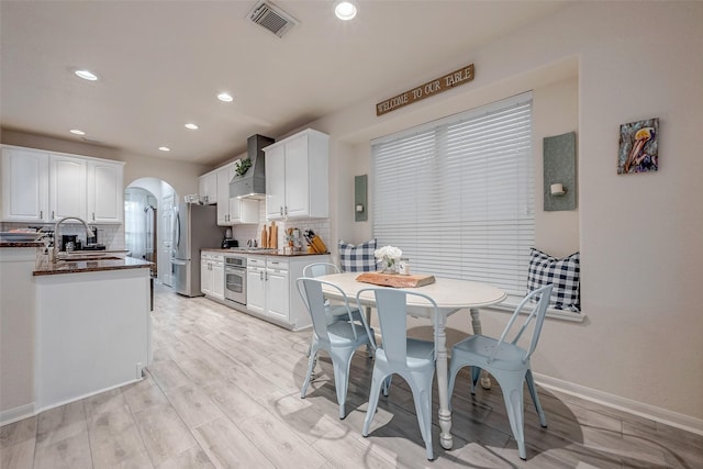 kitchen featuring visible vents, arched walkways, a sink, appliances with stainless steel finishes, and wall chimney exhaust hood