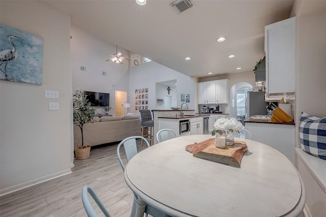 dining room with ceiling fan, sink, light hardwood / wood-style floors, and a towering ceiling