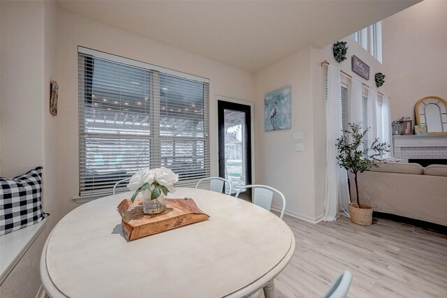 dining area with baseboards, light wood-style floors, and a fireplace