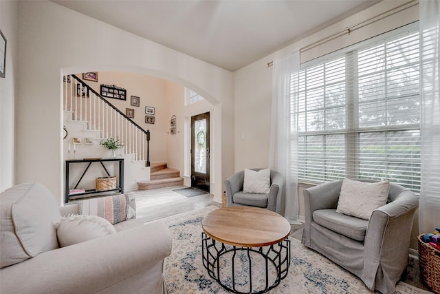 living area featuring arched walkways, stairway, and light wood-style floors