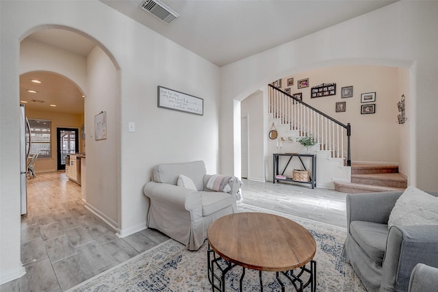 living area featuring visible vents, wood finish floors, baseboards, stairway, and arched walkways