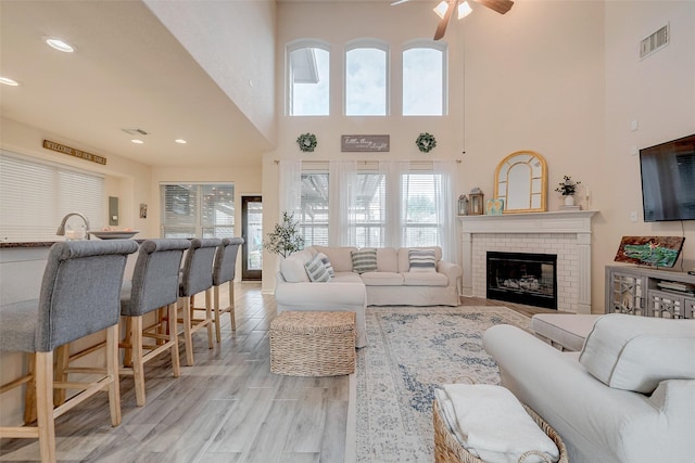 living area featuring light wood finished floors, visible vents, recessed lighting, and a brick fireplace