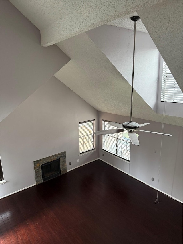 unfurnished living room with hardwood / wood-style flooring, ceiling fan, lofted ceiling, and a stone fireplace