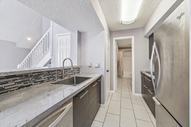 kitchen featuring stainless steel refrigerator, sink, decorative backsplash, light tile patterned floors, and light stone counters