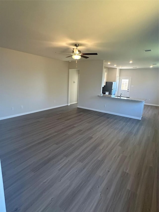 unfurnished living room featuring dark wood-type flooring and ceiling fan