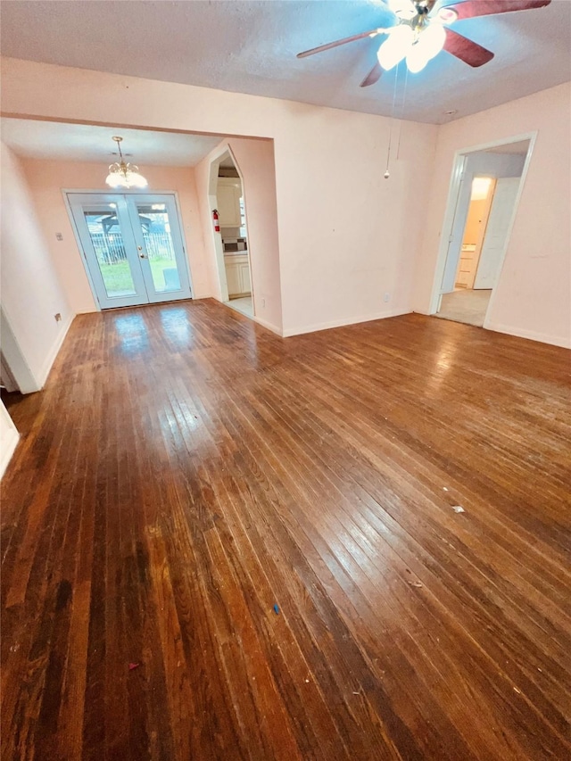 unfurnished living room featuring arched walkways, ceiling fan, dark wood-type flooring, and baseboards