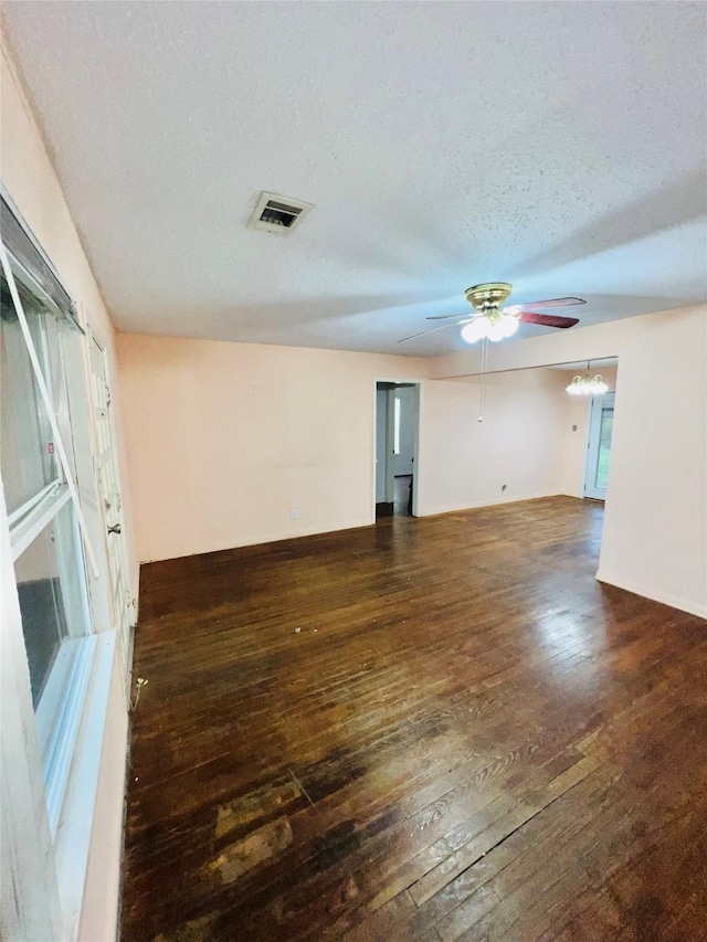 unfurnished room featuring dark wood-style floors, visible vents, a textured ceiling, baseboards, and ceiling fan with notable chandelier