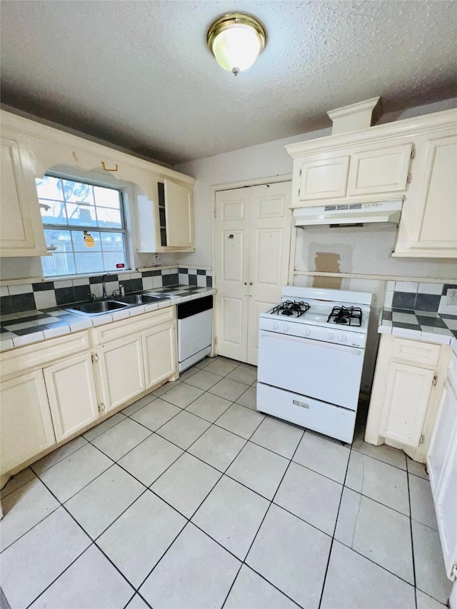 kitchen featuring a textured ceiling, under cabinet range hood, white appliances, a sink, and tile counters