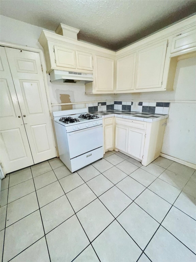 kitchen featuring white range with gas stovetop, under cabinet range hood, a textured ceiling, and light tile patterned floors