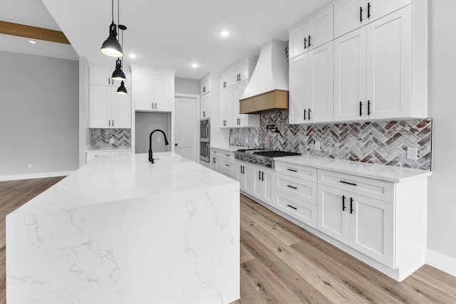 kitchen featuring white cabinets, stainless steel appliances, custom range hood, and a spacious island