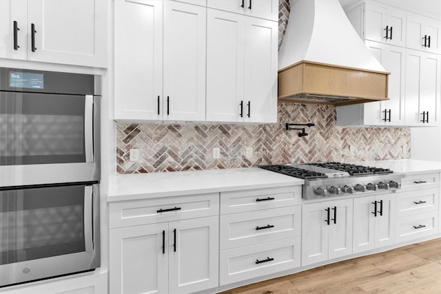 kitchen with white cabinetry, tasteful backsplash, custom range hood, and appliances with stainless steel finishes