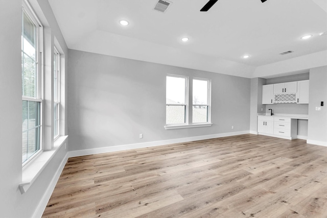 unfurnished living room featuring light hardwood / wood-style flooring, built in desk, and a healthy amount of sunlight