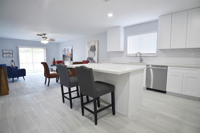 kitchen with a sink, a kitchen breakfast bar, a kitchen island, stainless steel dishwasher, and light countertops