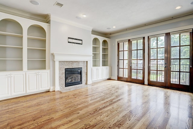 unfurnished living room featuring crown molding, built in shelves, a high end fireplace, and light hardwood / wood-style floors