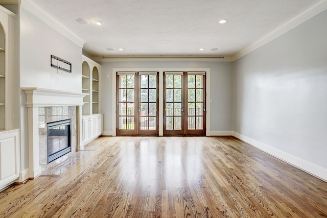 unfurnished living room with crown molding, a fireplace, light hardwood / wood-style floors, and built in shelves