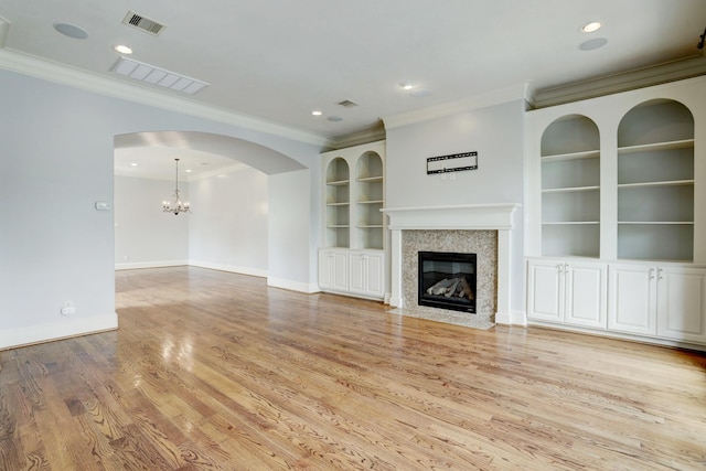 unfurnished living room featuring crown molding, a premium fireplace, built in shelves, and light wood-type flooring