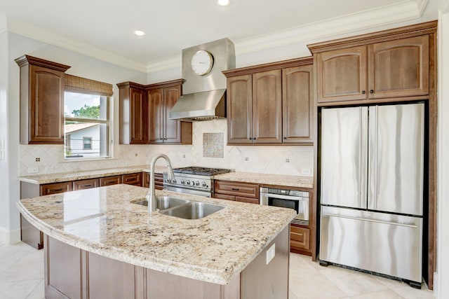 kitchen with wall chimney exhaust hood, sink, stainless steel appliances, light stone countertops, and a kitchen island with sink