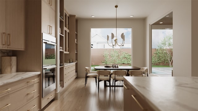 kitchen with pendant lighting, double oven, light wood-type flooring, light stone countertops, and an inviting chandelier