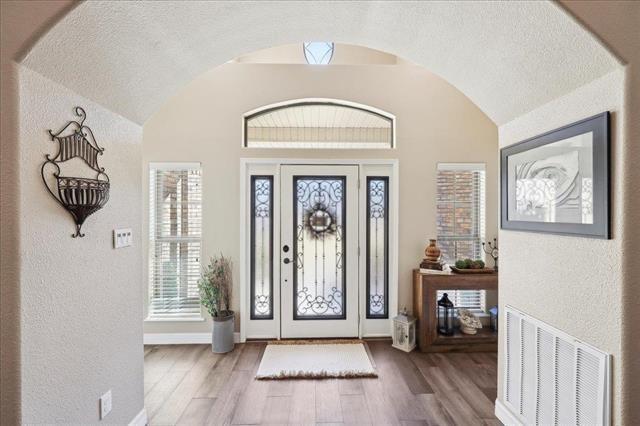 entrance foyer with vaulted ceiling, a textured ceiling, and light wood-type flooring