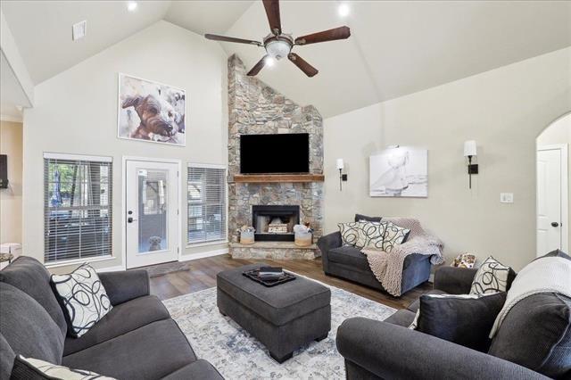 living room with hardwood / wood-style floors, a stone fireplace, high vaulted ceiling, and ceiling fan