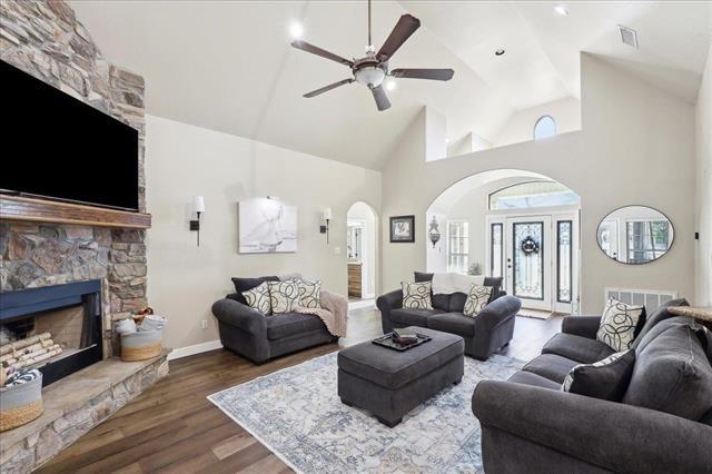 living room with ceiling fan, a stone fireplace, hardwood / wood-style floors, and high vaulted ceiling