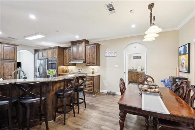 kitchen featuring appliances with stainless steel finishes, pendant lighting, decorative backsplash, ornamental molding, and light wood-type flooring