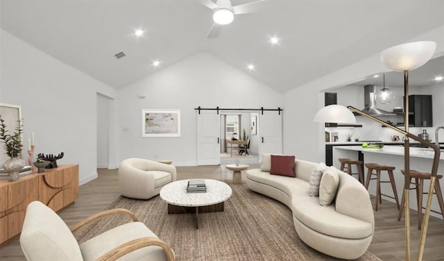 living room featuring wood-type flooring, high vaulted ceiling, a barn door, and ceiling fan