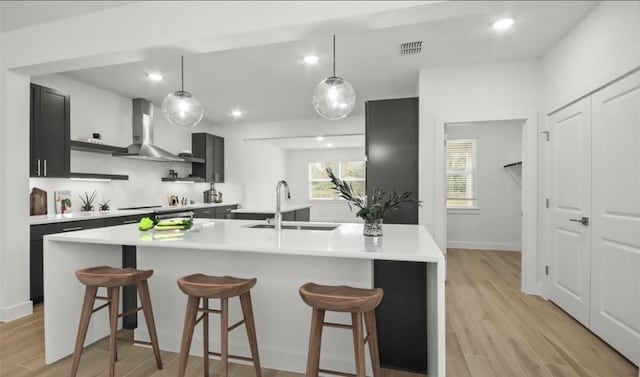 kitchen with a kitchen breakfast bar, sink, a center island with sink, and wall chimney range hood