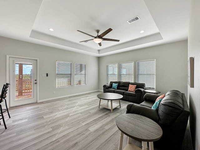 living room with a raised ceiling, ceiling fan, and light wood-type flooring