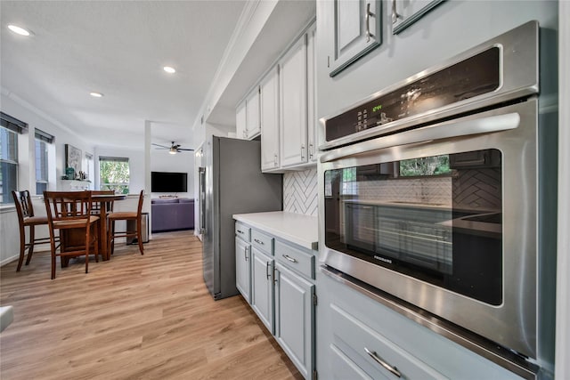 kitchen with tasteful backsplash, ornamental molding, appliances with stainless steel finishes, light hardwood / wood-style floors, and white cabinets