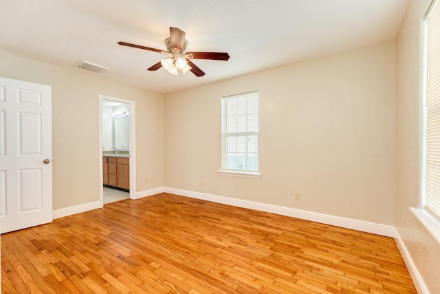 unfurnished bedroom with ceiling fan, ensuite bath, multiple windows, and light wood-type flooring