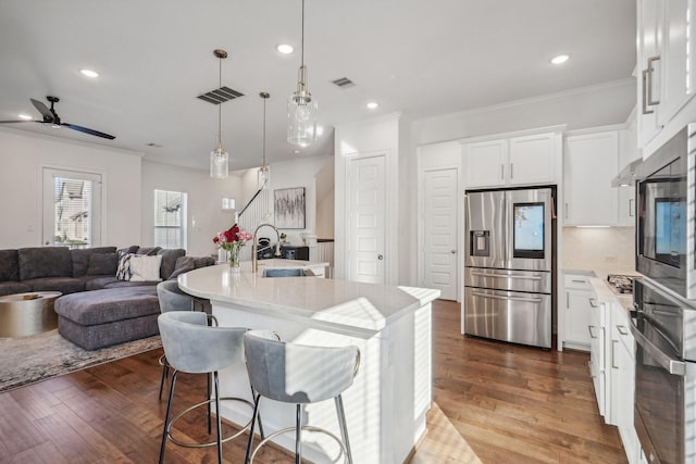 kitchen with decorative light fixtures, white cabinetry, sink, stainless steel appliances, and a center island with sink