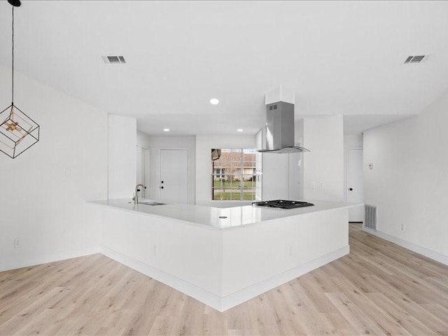 kitchen with island range hood, sink, hanging light fixtures, kitchen peninsula, and light hardwood / wood-style flooring