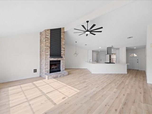 unfurnished living room featuring ceiling fan, a fireplace, lofted ceiling with beams, and light wood-type flooring