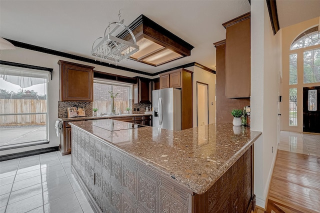 kitchen with light stone countertops, a wealth of natural light, stainless steel fridge, and backsplash