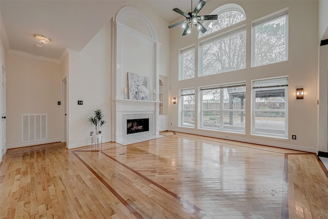 unfurnished living room featuring built in features, a towering ceiling, ornamental molding, light hardwood / wood-style floors, and a tiled fireplace