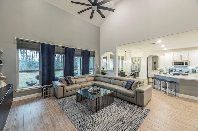 living room with sink, light hardwood / wood-style flooring, high vaulted ceiling, and ceiling fan