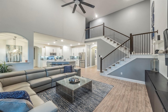 living room featuring a towering ceiling, sink, ceiling fan with notable chandelier, and light hardwood / wood-style flooring