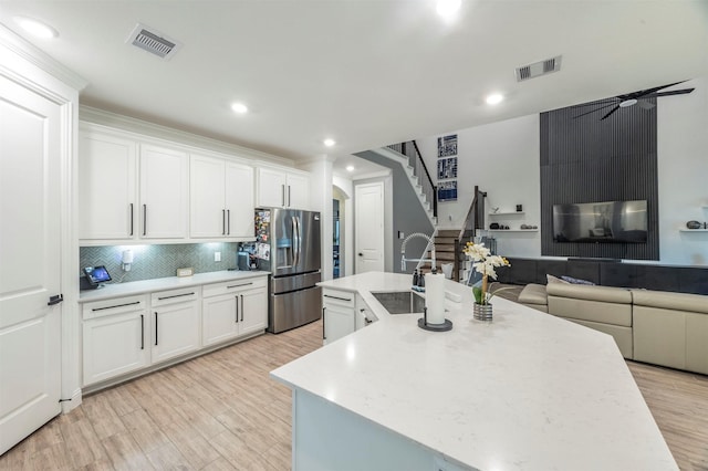 kitchen featuring tasteful backsplash, white cabinetry, a kitchen island with sink, and stainless steel fridge