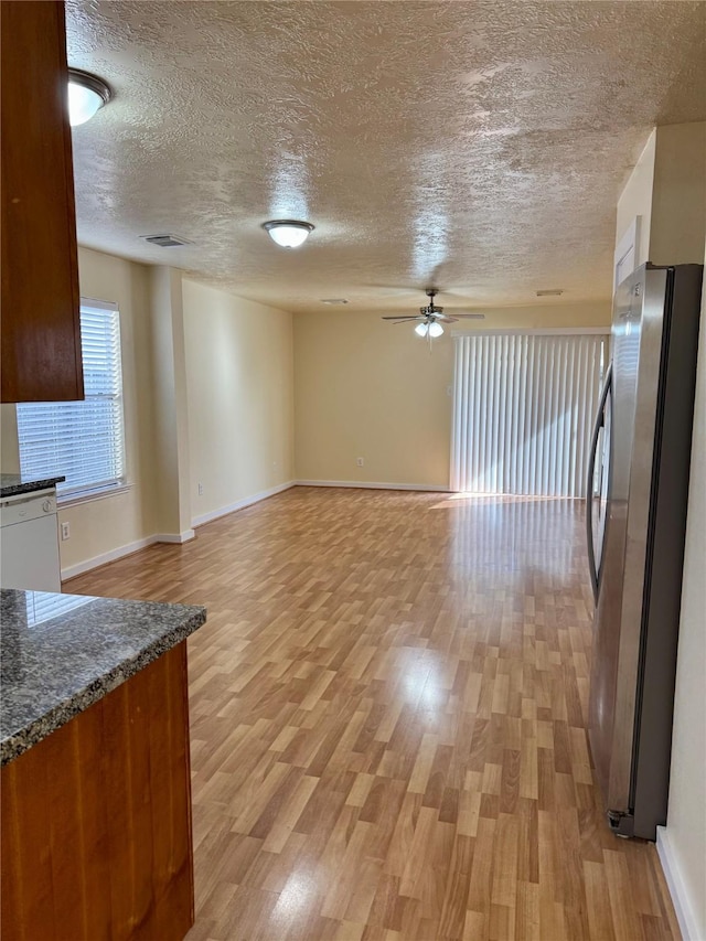 kitchen featuring stainless steel refrigerator, ceiling fan, dark stone countertops, white dishwasher, and light wood-type flooring