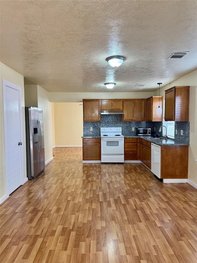 kitchen featuring decorative light fixtures, sink, backsplash, stainless steel appliances, and light wood-type flooring