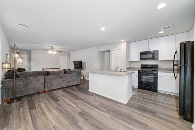 kitchen with an island with sink, hardwood / wood-style floors, white cabinets, and black appliances