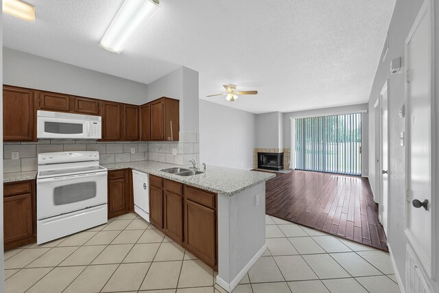 kitchen with light tile patterned flooring, sink, backsplash, kitchen peninsula, and white appliances